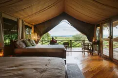 Safari tent interior at Katavi Wildlife Camp with bed and veranda overlooking the plains